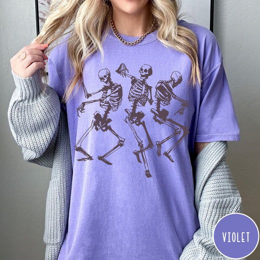 Comfort Colors tee in Violet featuring dancing skeletons graphic illustration on the front of the shirt