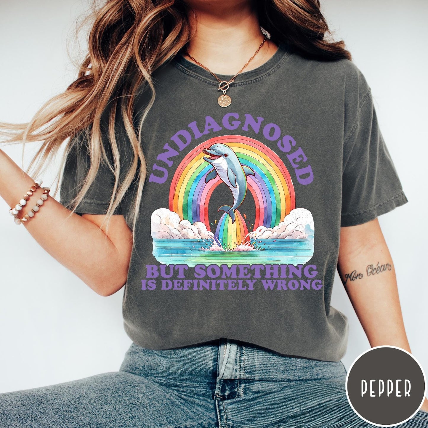 Comfort Colors tee in Pepper featuring graphic style illustration of a dolphin jumping through a colorful rainbow