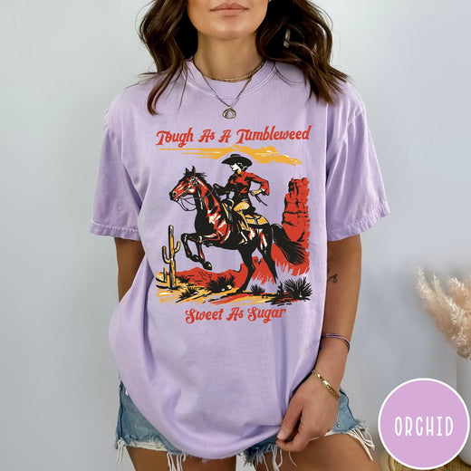 Comfort Colors tee in Orchid featuring western style graphic of a cowgirl riding a horse in desert