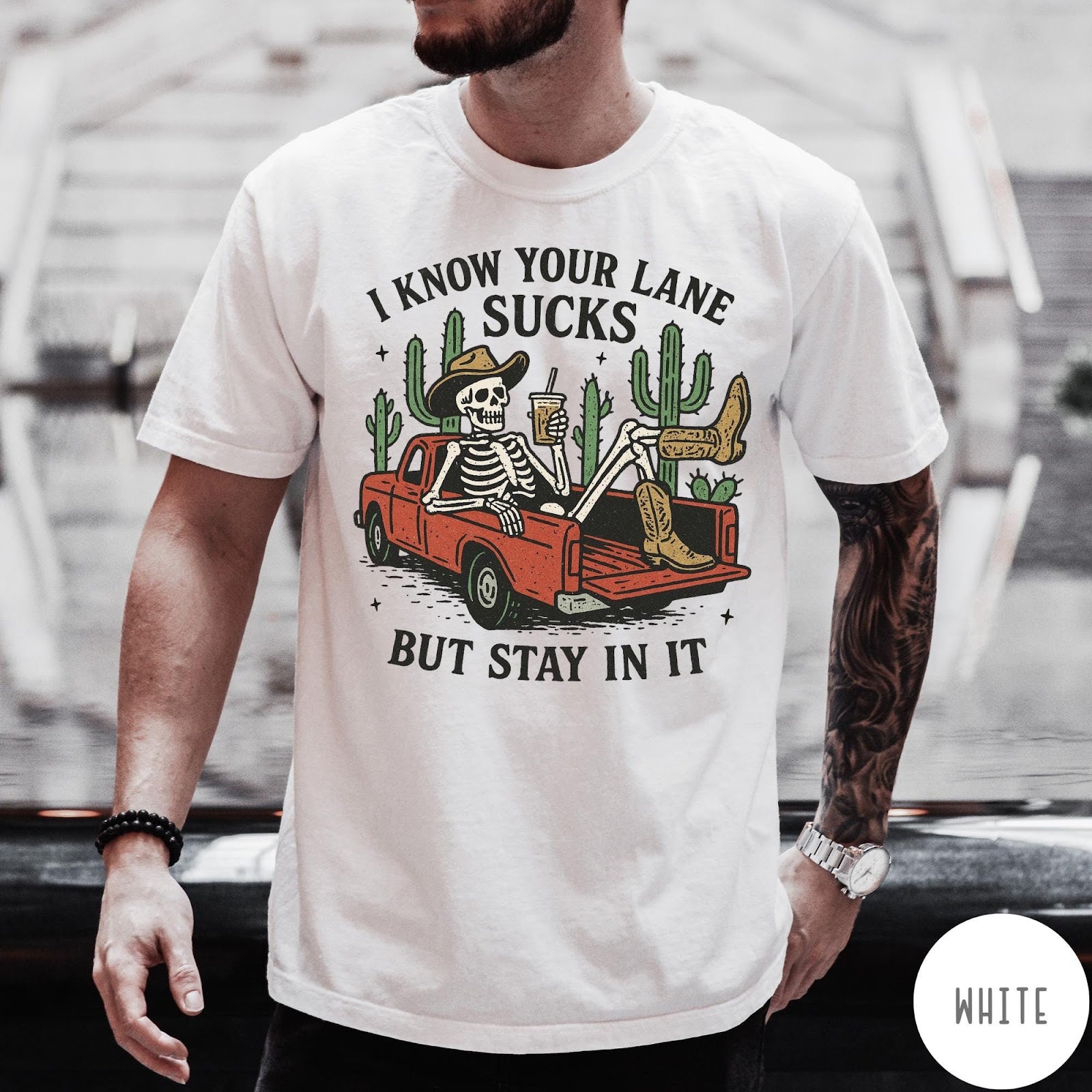 Comfort Colors tee in White featuring western skeleton graphic with cowboy hat and boots in pickup truck