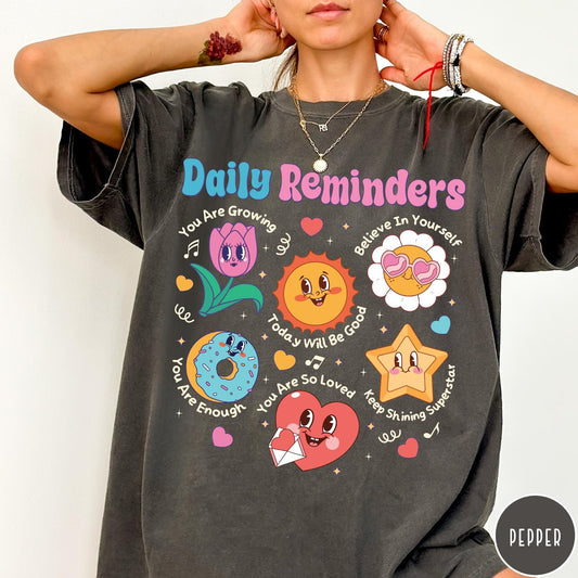 Comfort Colors tee in Pepper featuring retro mascot design with daily affirmations and colorful cartoon characters