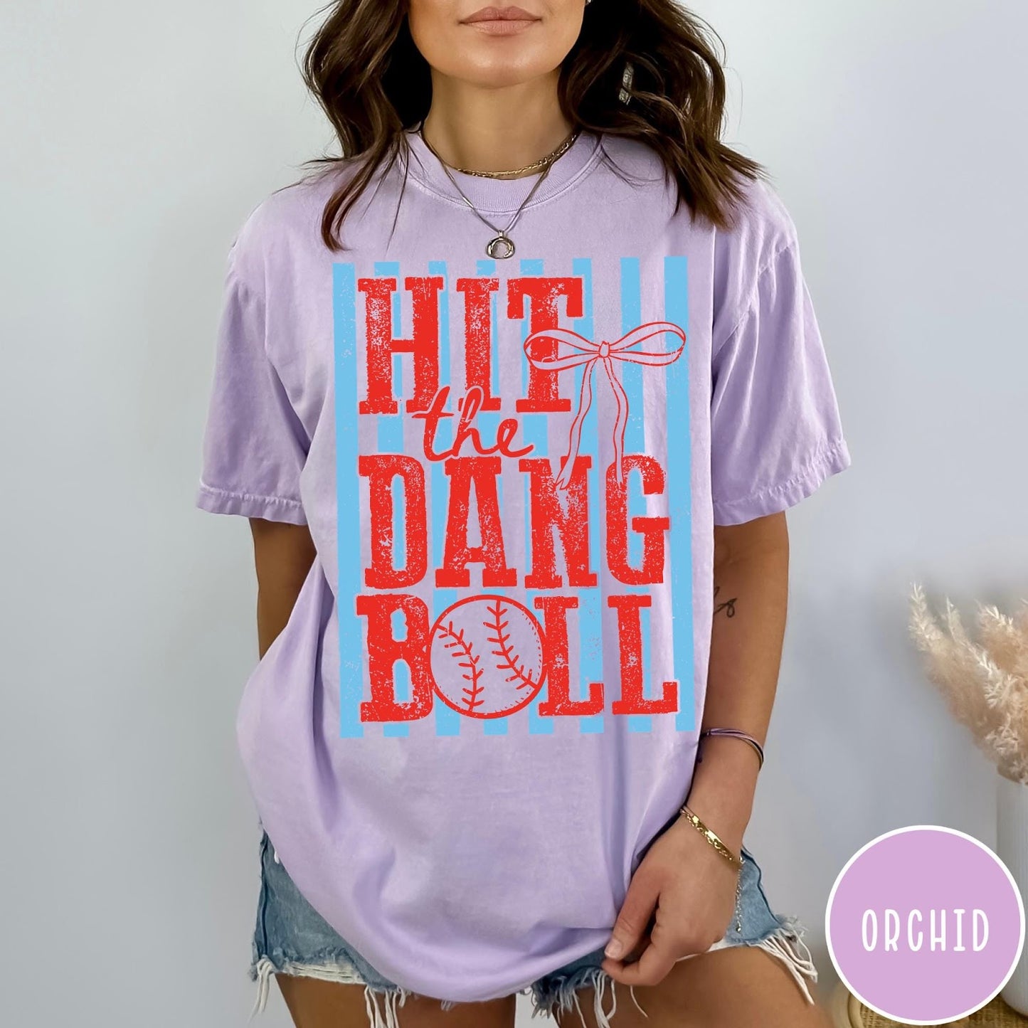 Comfort Colors tee in Orchid featuring baseball design with red text and a blue striped background graphic