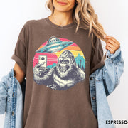 Comfort Colors tee in Espresso featuring retro graphic design of Bigfoot taking a selfie with a UFO