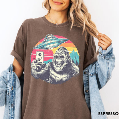 Comfort Colors tee in Espresso featuring retro graphic design of Bigfoot taking a selfie with a UFO