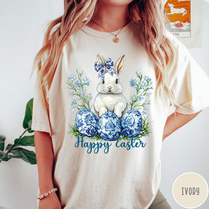 Comfort Colors tee in Ivory featuring Easter bunny graphic with blue floral bow and patterned Easter eggs