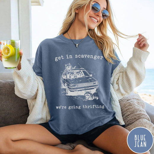 Comfort Colors tee in Blue Jean featuring illustrated style graphic of raccoons riding in a car and thrifting