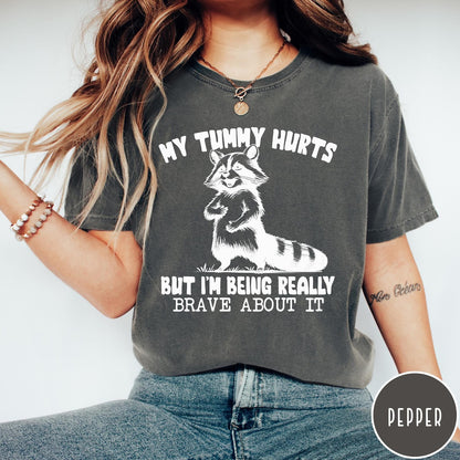 Comfort Colors tee in Pepper featuring graphic illustration of a standing raccoon with funny text about being brave