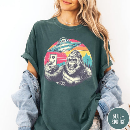Comfort Colors tee in Blue Spruce featuring retro graphic design of Bigfoot taking a selfie with a UFO