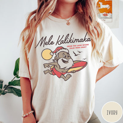 Comfort Colors tee in Ivory featuring vintage style graphic of a surfing Santa Claus on vacation