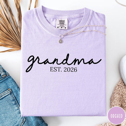 Comfort Colors tee in Orchid featuring script design Grandma Est. 2026 announcement graphic in black