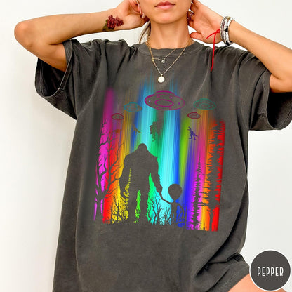 Comfort Colors tee in Pepper featuring a vibrant graphic of Bigfoot and an alien holding hands in forest