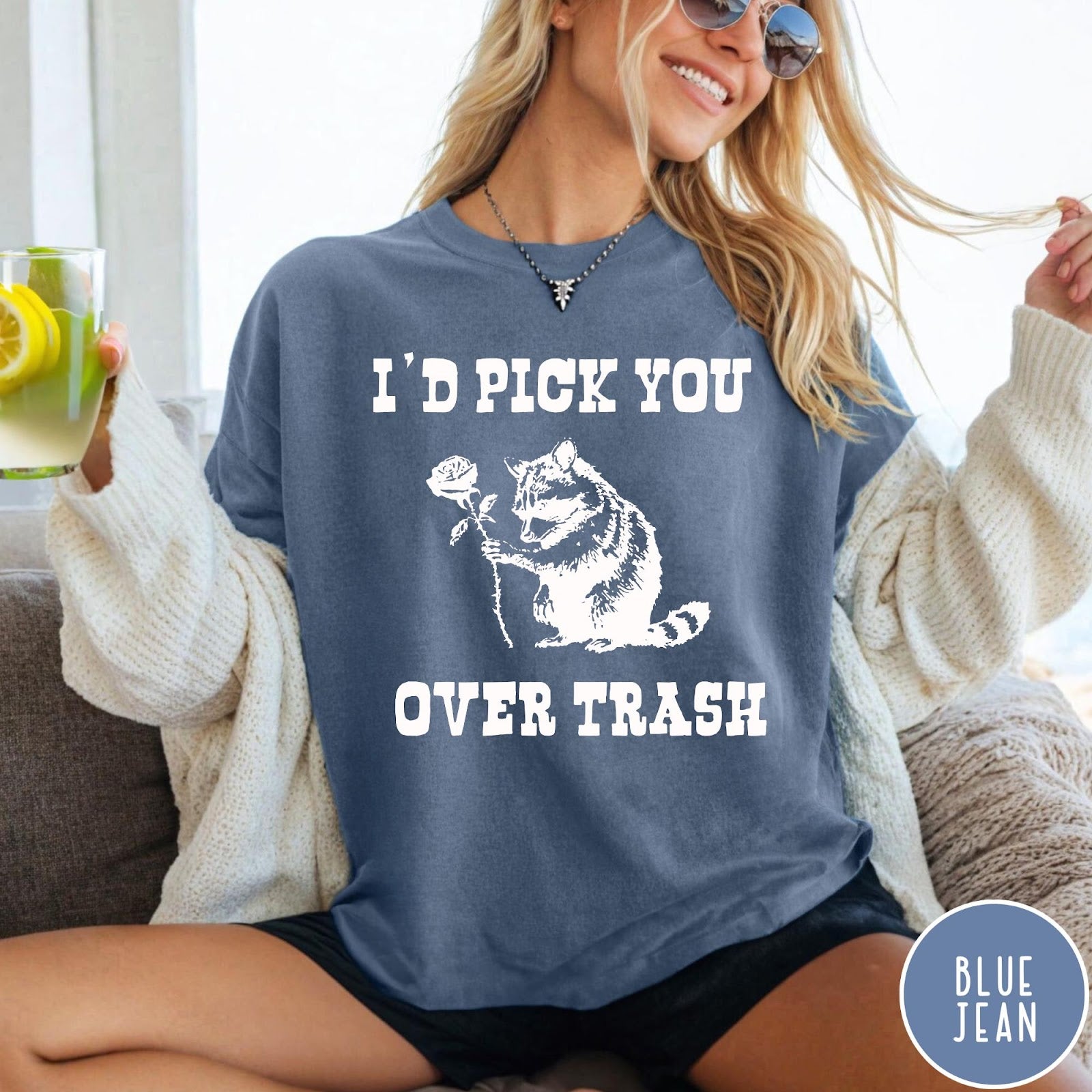 Comfort Colors tee in Blue Jean featuring a whimsical graphic of a raccoon holding a white rose.