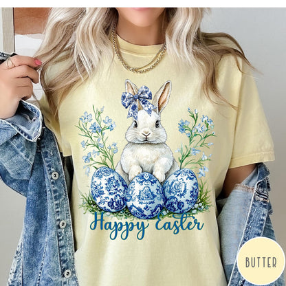 Comfort Colors tee in Butter featuring Easter bunny graphic with blue floral bow and patterned Easter eggs