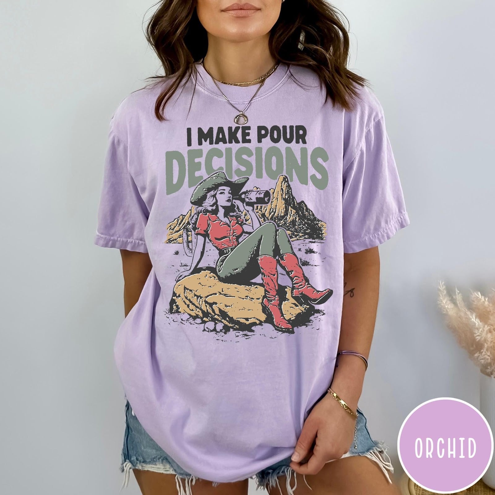 Comfort Colors tee in Orchid featuring western style graphic of a cowgirl sitting on a rock drinking