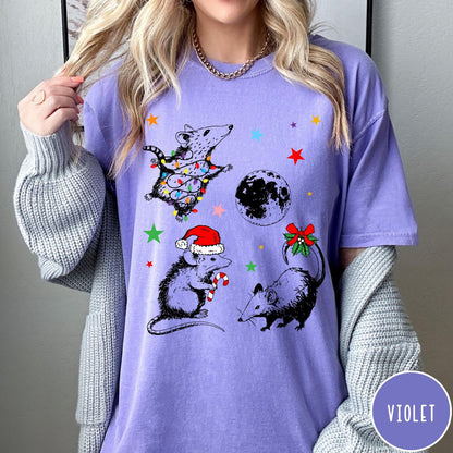 Comfort Colors tee in Violet featuring holiday possum graphic with Christmas lights, candy cane, and moon.