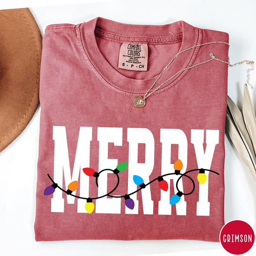Comfort Colors tee in Crimson featuring holiday style graphic with white Merry text and colorful Christmas lights