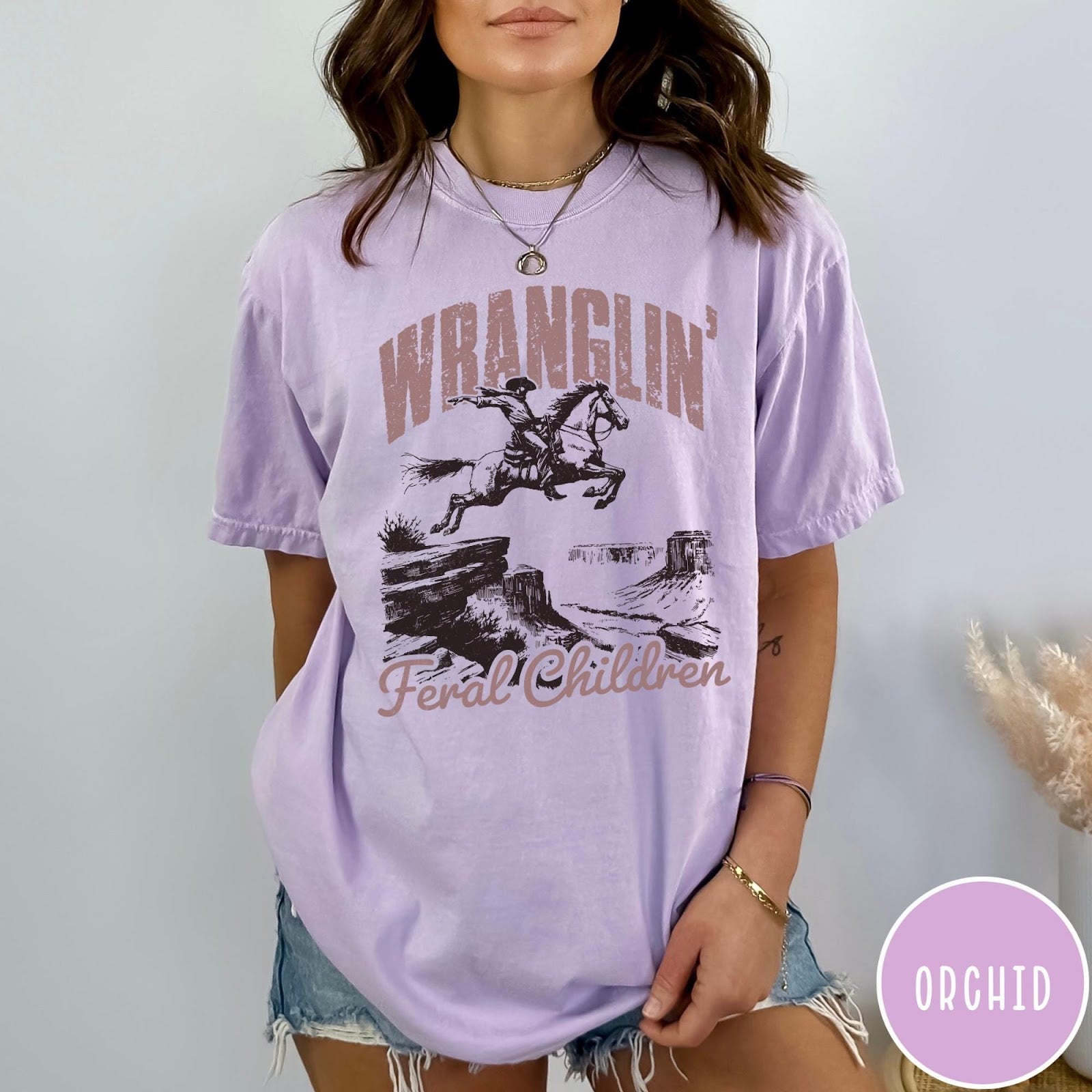 Comfort Colors tee in Orchid featuring western style graphic of a cowboy on horseback jumping a canyon