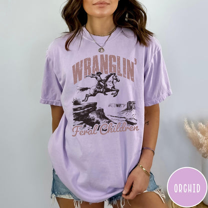 Comfort Colors tee in Orchid featuring western style graphic of a cowboy on horseback jumping a canyon