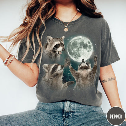 Comfort Colors tee in Pepper featuring artistic graphic of three raccoons reaching toward a bright full moon