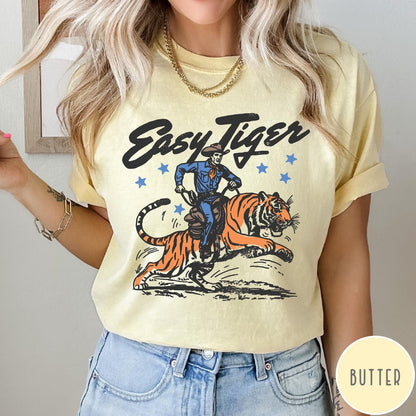 Comfort Colors tee in Butter featuring western graphic style cowboy riding a tiger with blue stars