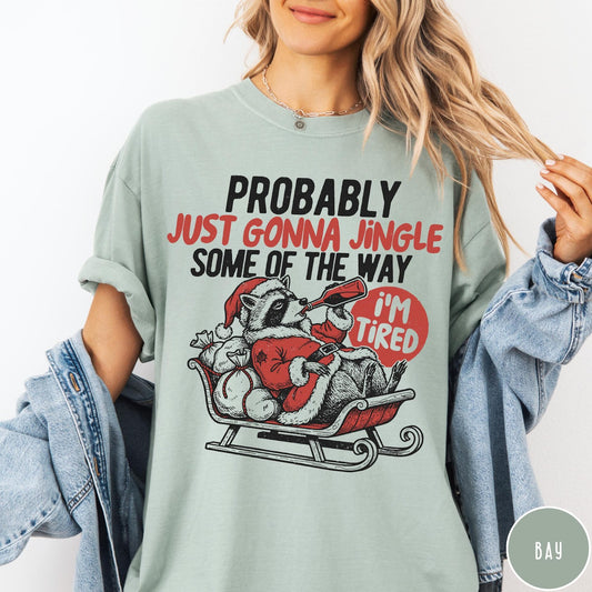 Comfort Colors tee in Bay featuring vintage style graphic of a tired raccoon in a Santa sleigh