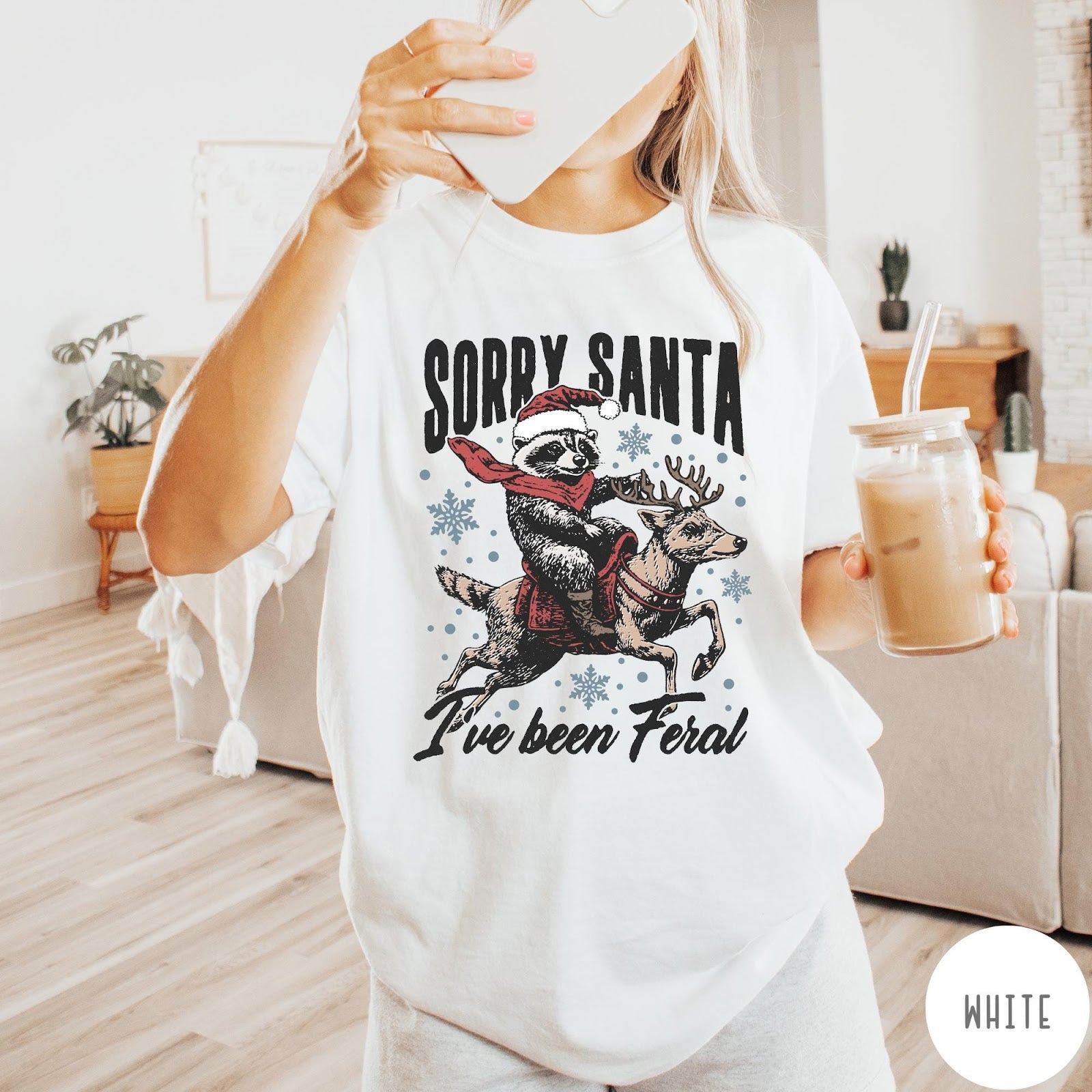 Comfort Colors tee in White featuring festive graphic of a raccoon wearing a Santa hat riding a reindeer