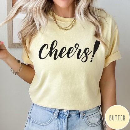 Comfort Colors tee in Butter featuring New Year celebration graphic with black cheers text and champagne bottle