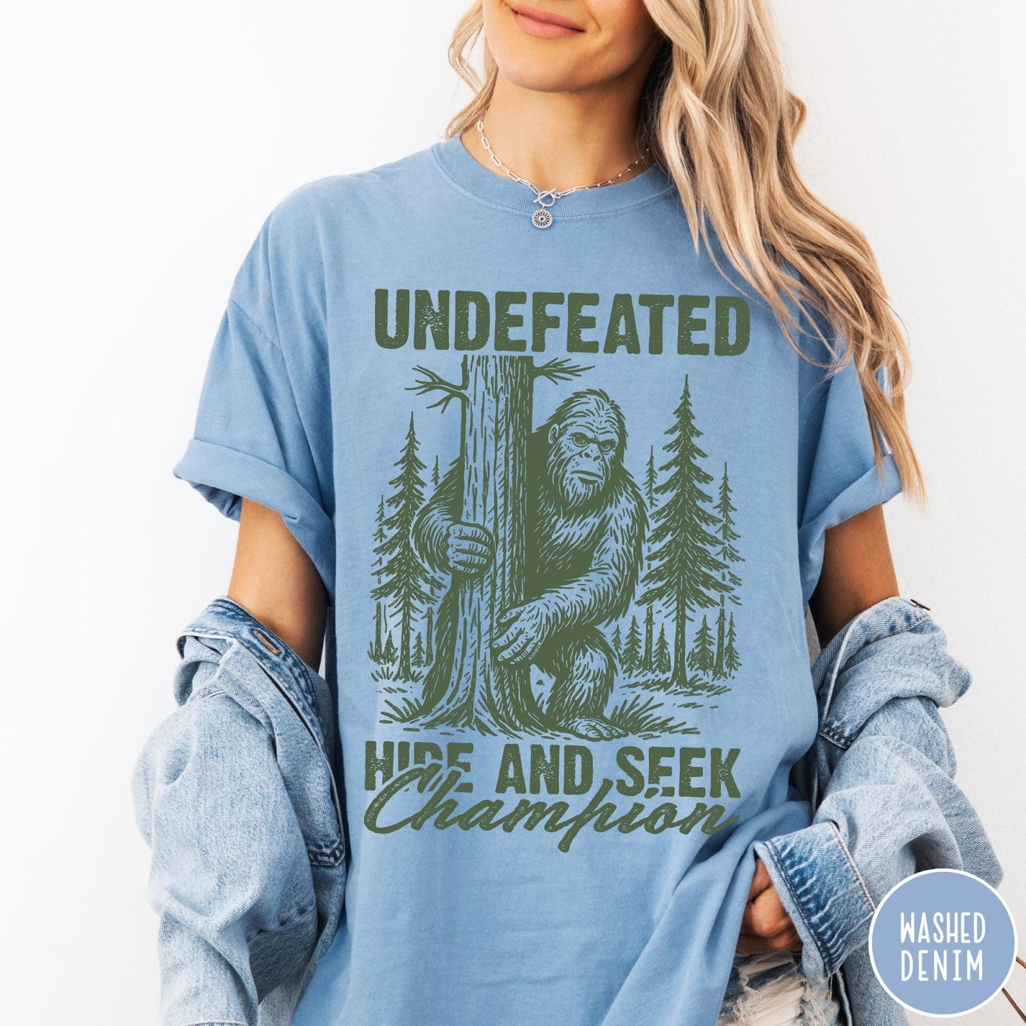 Comfort Colors tee in Washed Denim featuring vintage style graphic of Bigfoot hiding behind a large pine tree