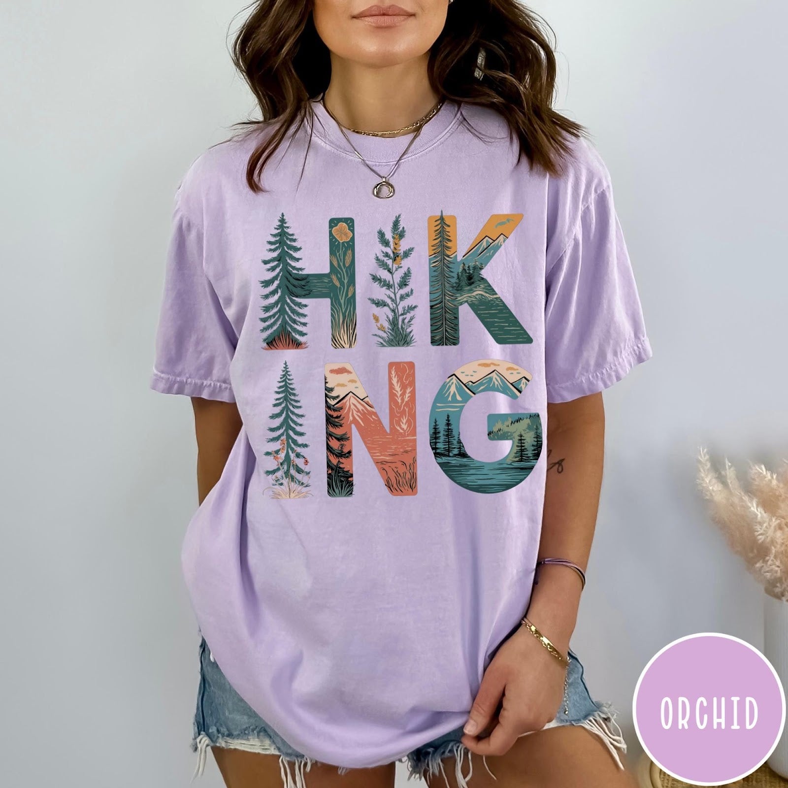 Comfort Colors tee in Orchid featuring nature graphic with trees and mountains inside the word Hiking