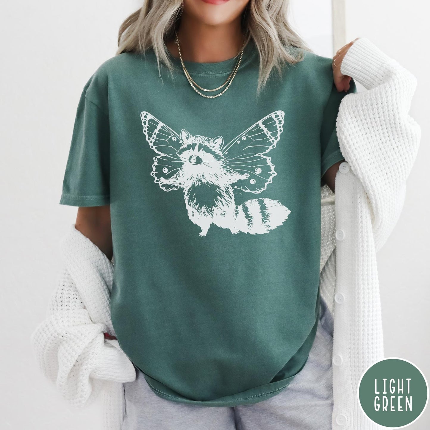 Comfort Colors tee in Light Green featuring whimsical graphic style of a raccoon with large detailed butterfly wings