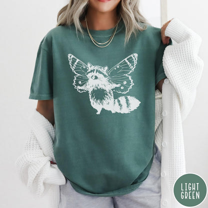 Comfort Colors tee in Light Green featuring whimsical graphic style of a raccoon with large detailed butterfly wings