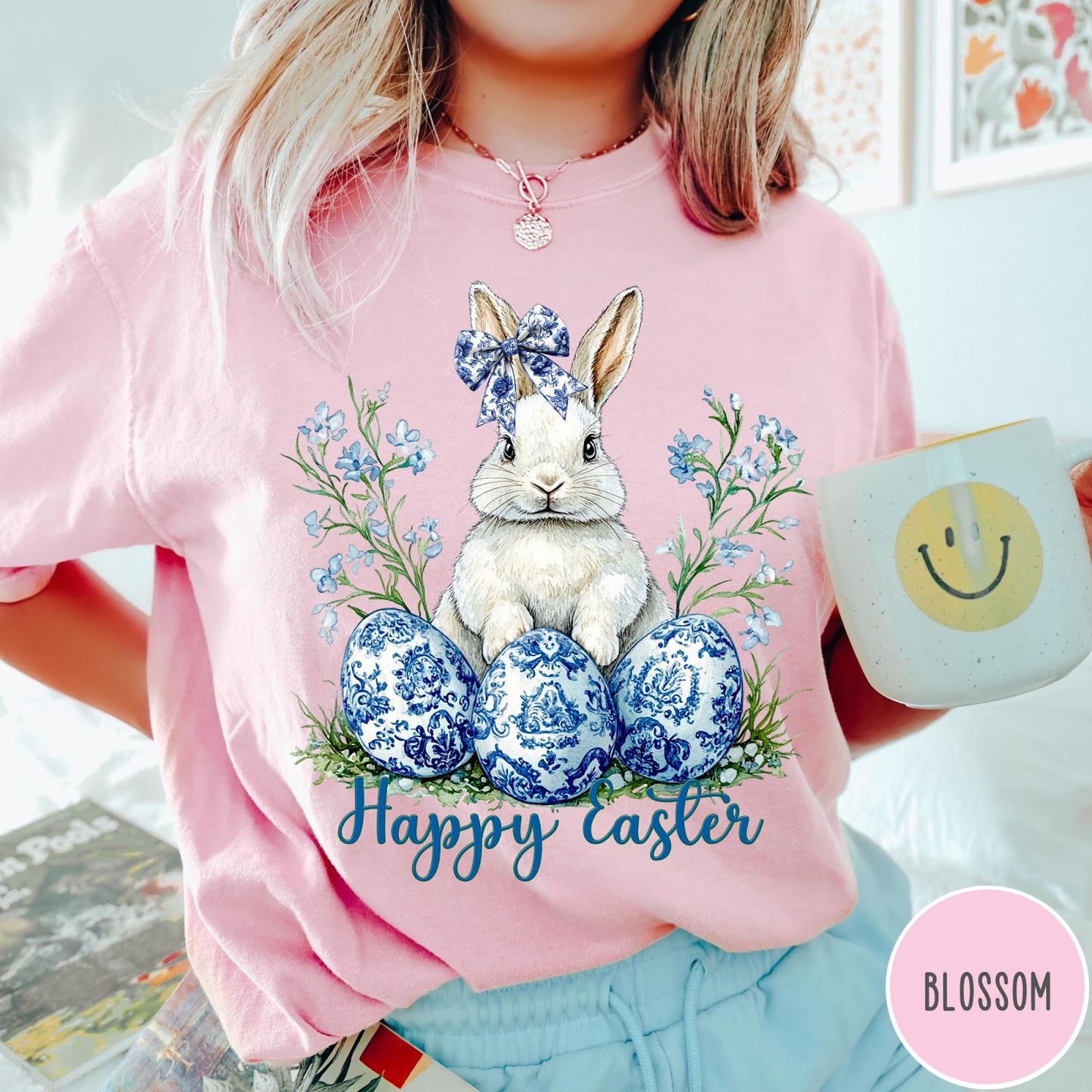 Comfort Colors tee in Blossom featuring Easter bunny graphic with blue floral bow and patterned Easter eggs