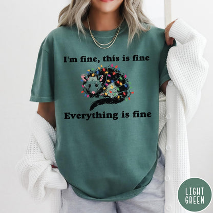 Comfort Colors tee in Light Green featuring graphic illustration of an opossum tangled in colorful Christmas lights