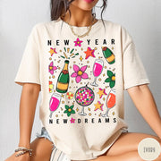 Comfort Colors tee in Ivory featuring New Year celebration graphic with champagne bottles, glasses, and disco ball