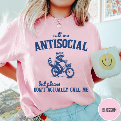 Comfort Colors tee in Blossom featuring graphic style illustration of a raccoon riding a bicycle
