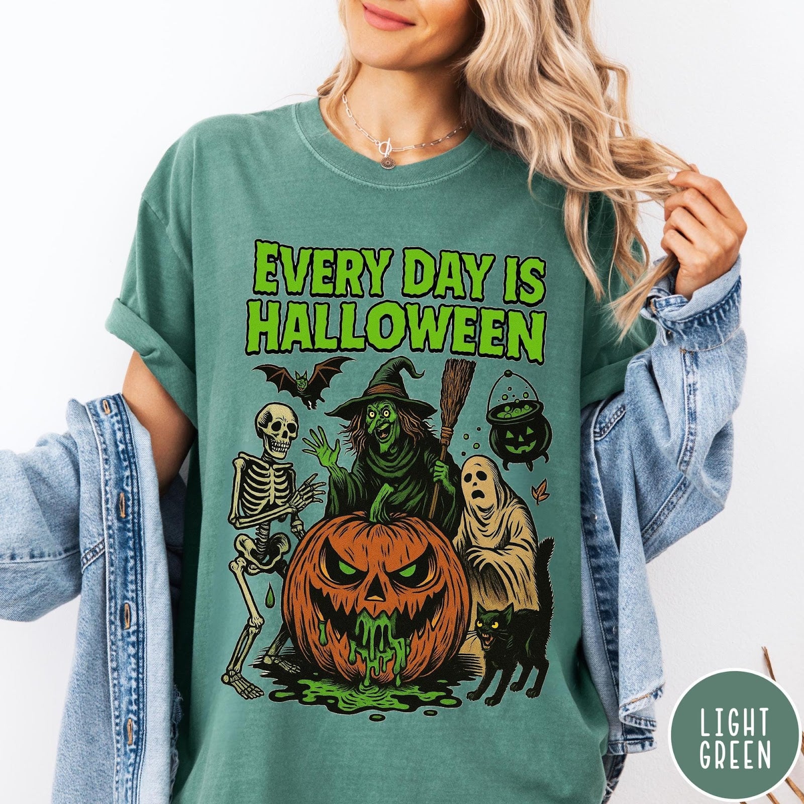 Comfort Colors tee in Light Green featuring Halloween graphic with a witch, skeleton, ghost, and a dripping pumpkin.