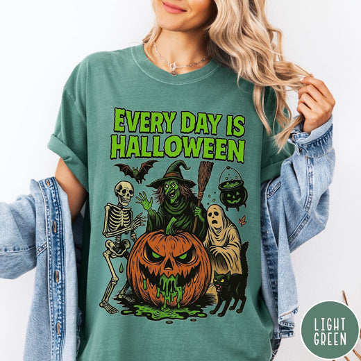 Comfort Colors tee in Light Green featuring Halloween graphic with a witch, skeleton, ghost, and a dripping pumpkin.