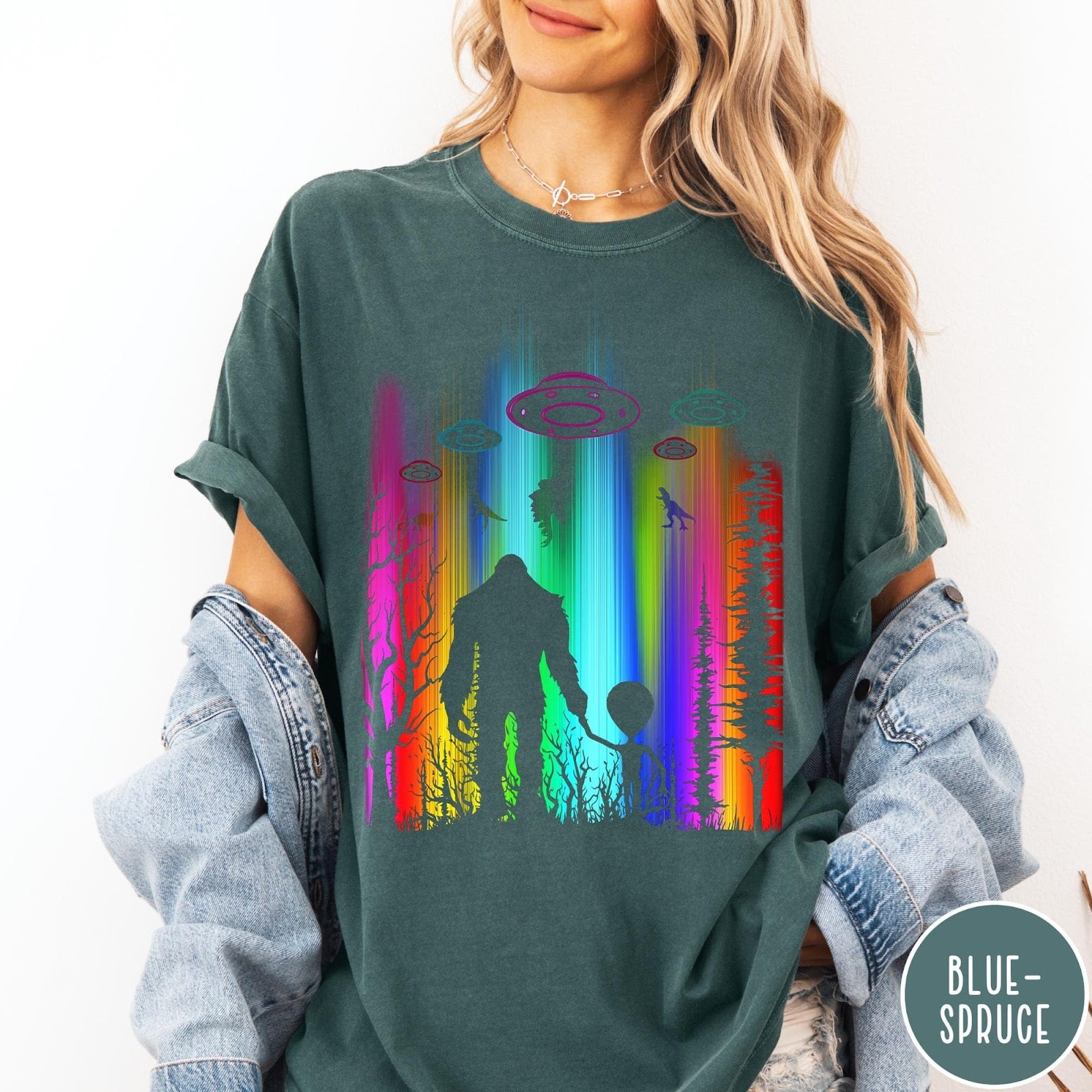 Comfort Colors tee in Blue Spruce featuring a vibrant graphic of Bigfoot and an alien holding hands in forest