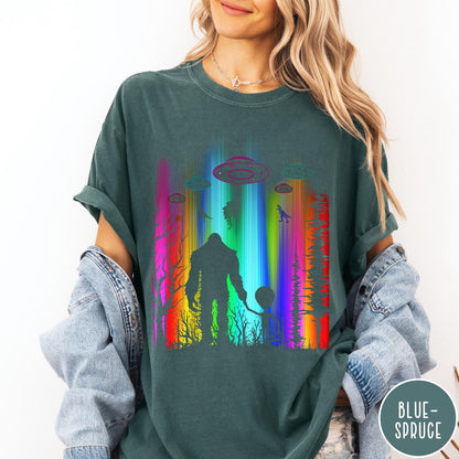 Comfort Colors tee in Blue Spruce featuring a vibrant graphic of Bigfoot and an alien holding hands in forest