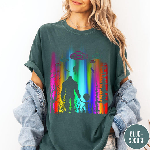Comfort Colors tee in Blue Spruce featuring a vibrant graphic of Bigfoot and an alien holding hands in forest