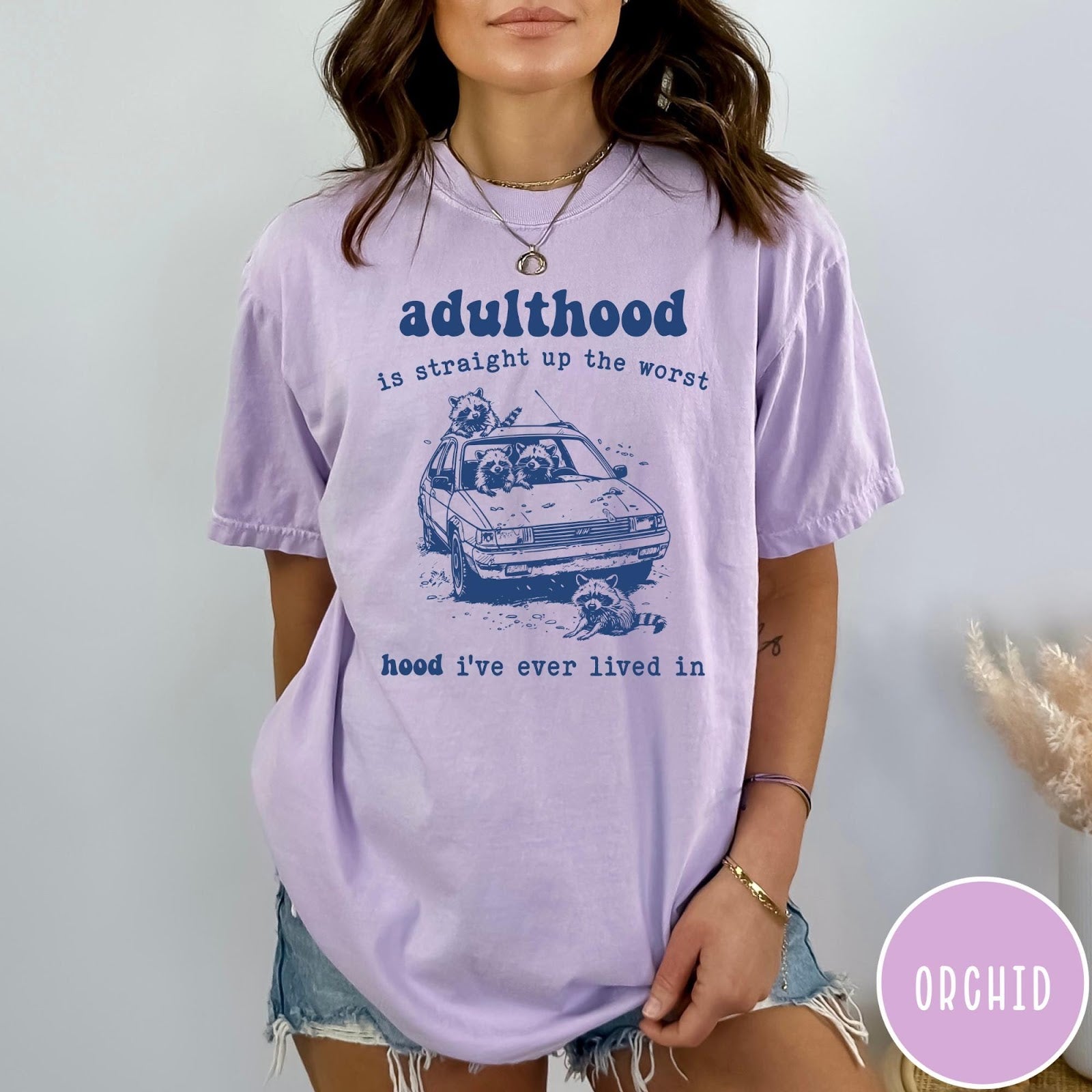 Comfort Colors tee in Orchid featuring illustrated style graphic of raccoons sitting in and around a car