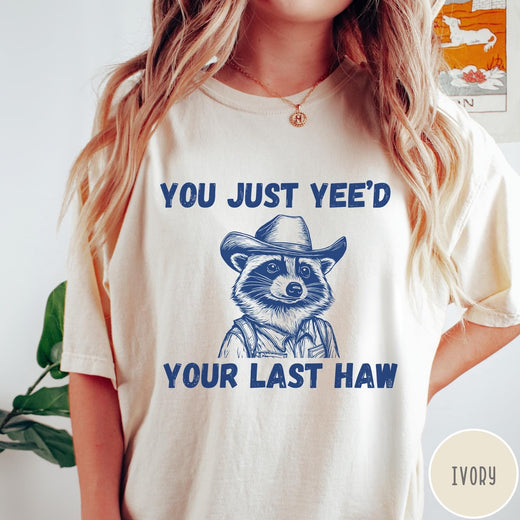 Comfort Colors tee in Ivory featuring western style graphic of a raccoon wearing a cowboy hat