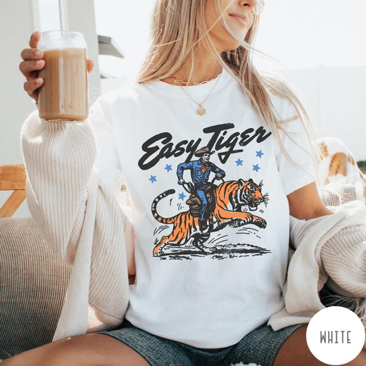 Comfort Colors tee in White featuring western graphic style cowboy riding a tiger with blue stars