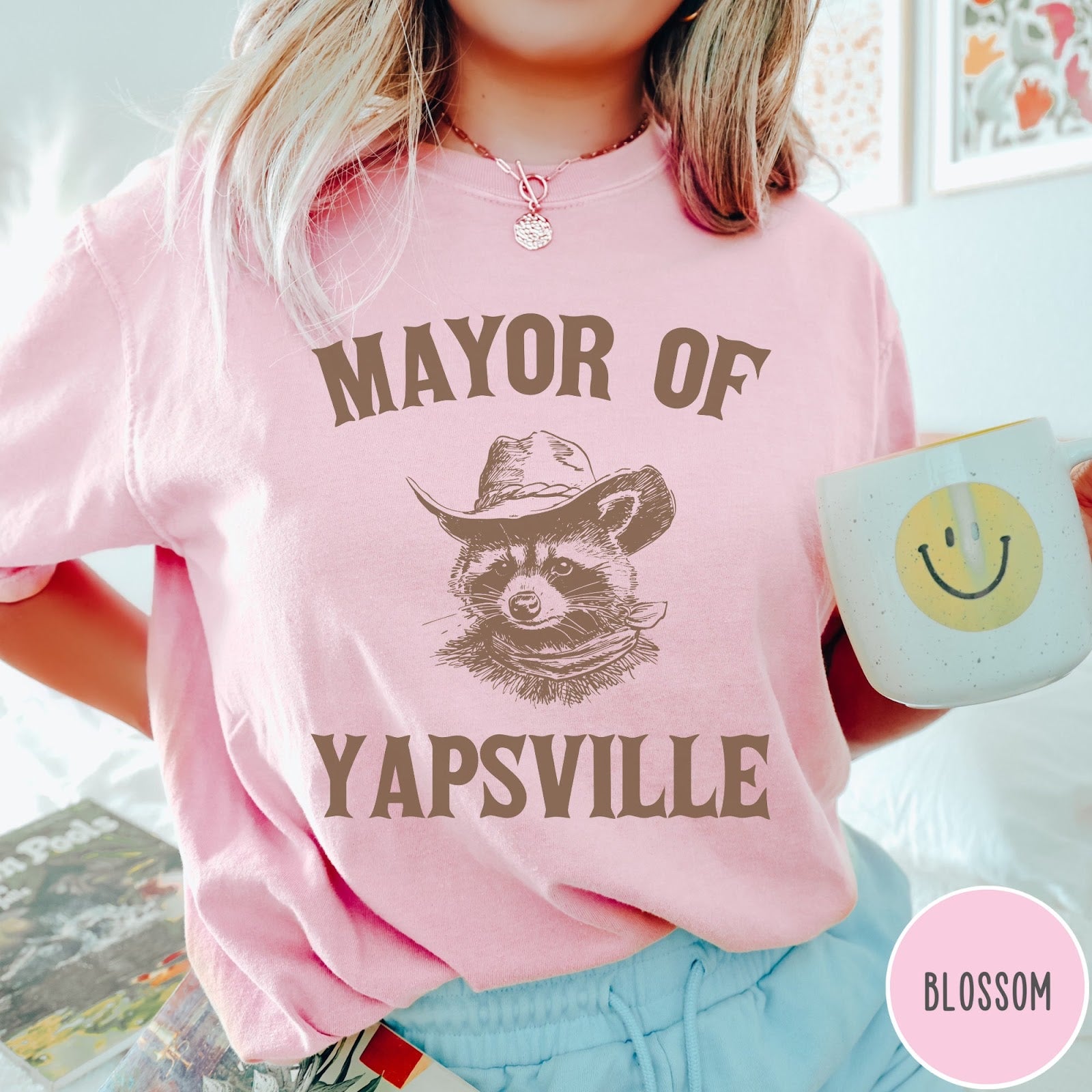 Comfort Colors tee in Blossom featuring western style graphic of a raccoon wearing a cowboy hat and bandana