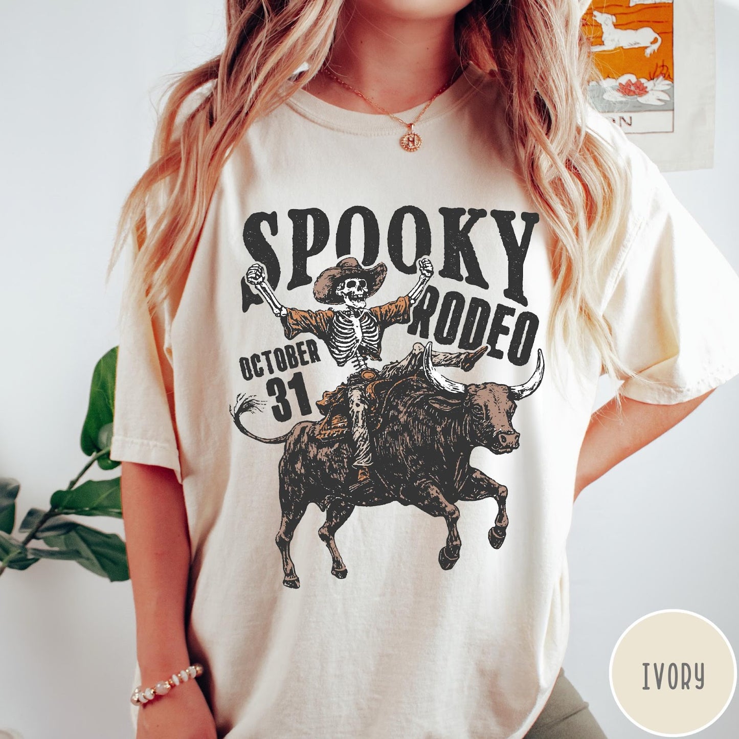 Comfort Colors tee in Ivory featuring western style graphic of a skeleton cowboy riding a bucking bull