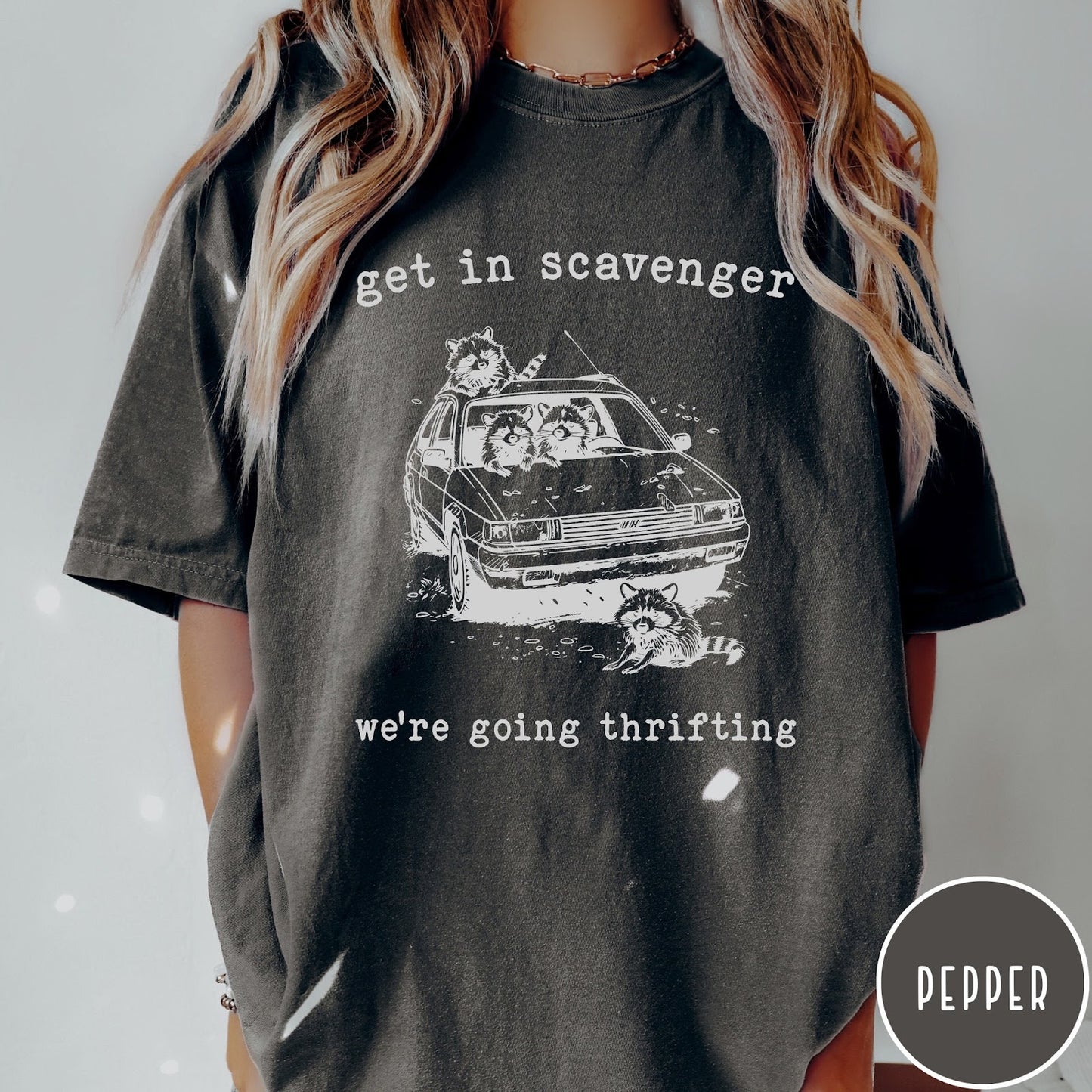 Comfort Colors tee in Pepper featuring illustrated style graphic of raccoons riding in a car and thrifting