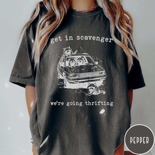 Comfort Colors tee in Pepper featuring illustrated style graphic of raccoons riding in a car and thrifting