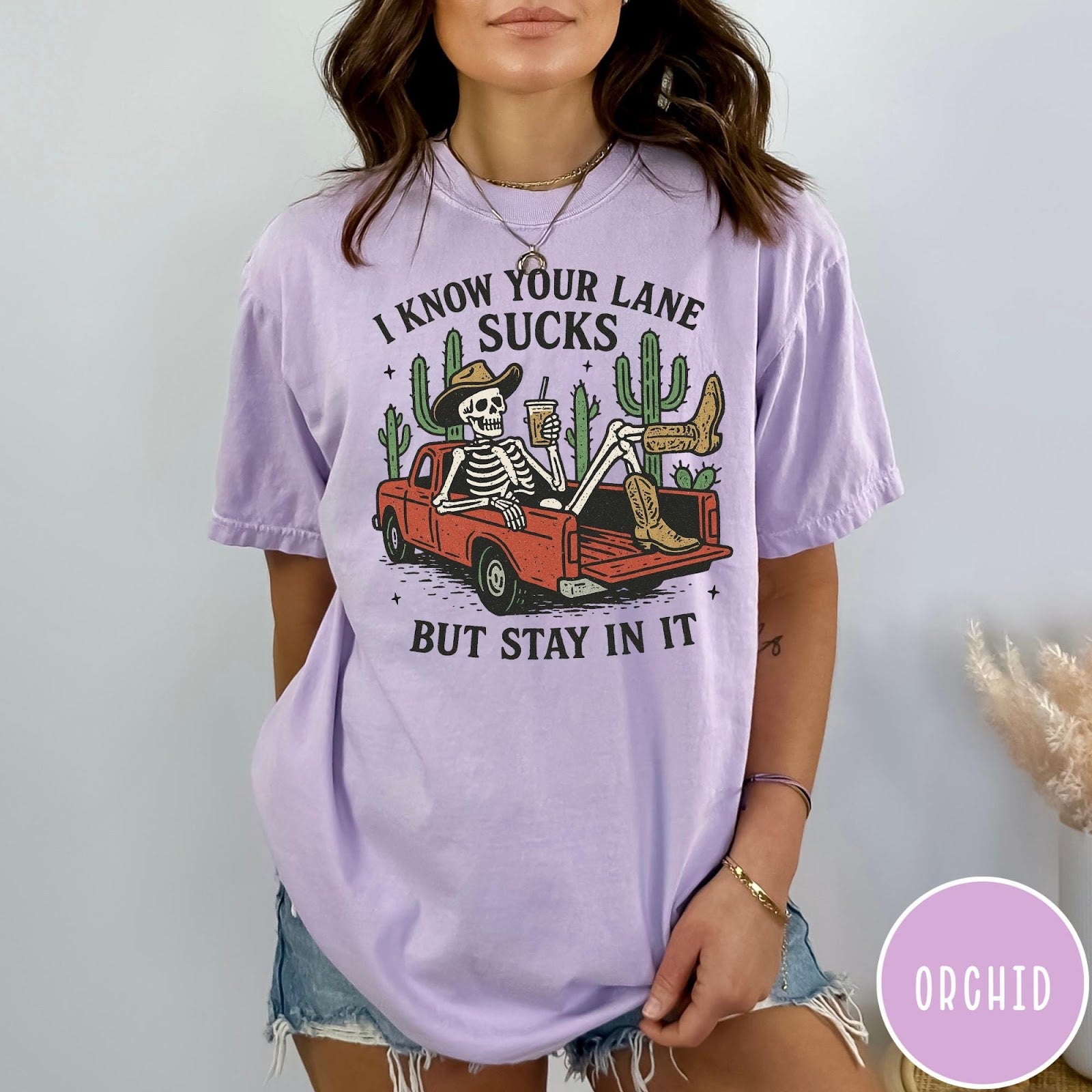 Comfort Colors tee in Orchid featuring western skeleton design with cowboy hat and boots in truck bed