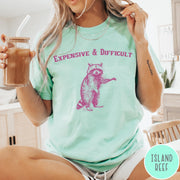 Comfort Colors tee in Island Reef featuring vintage style graphic of a standing raccoon with text Expensive and Difficult
