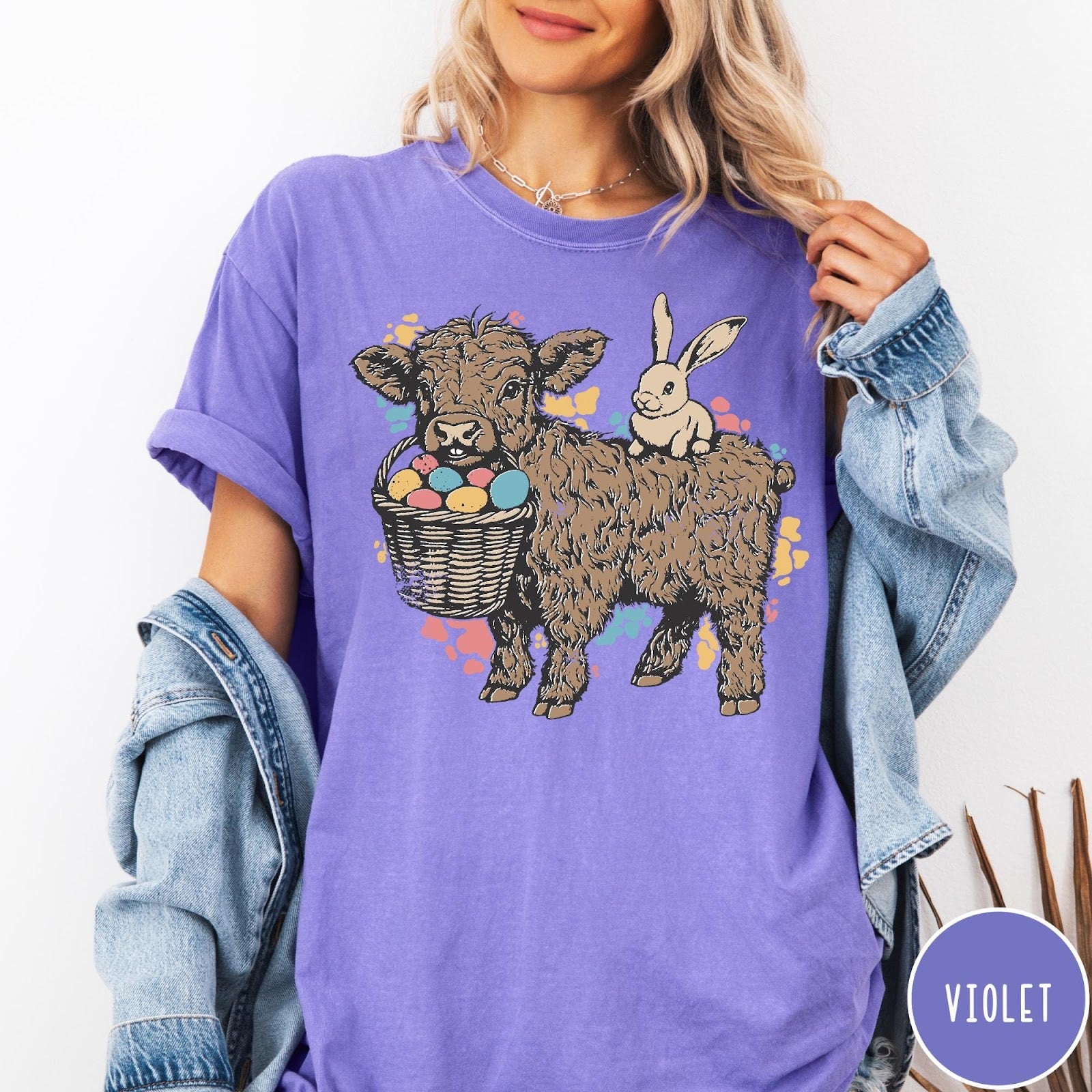 Comfort Colors tee in Violet featuring graphic style illustration of a Highland cow with bunny and eggs